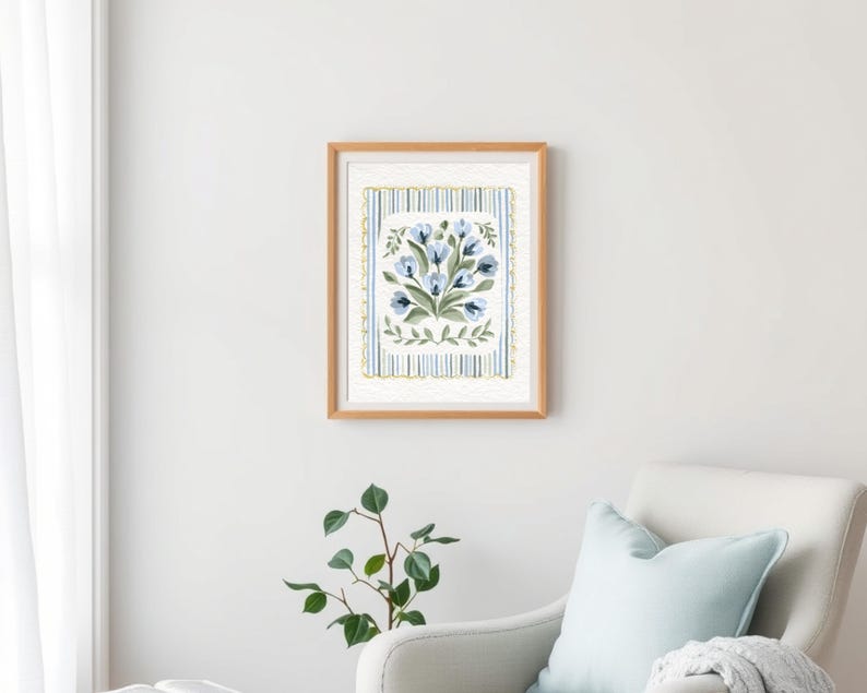 Puede incluir: Una impresi&oacute;n en acuarela enmarcada que presenta un ramo de flores azules con hojas verdes. La obra de arte est&aacute; sobre un fondo a rayas con detalles en azul y dorado, dentro de un marco de madera marr&oacute;n claro. La impresi&oacute;n se exhibe en una pared blanca.