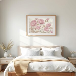 May include: A framed floral print featuring pink roses hangs above a bed with white bedding and a tan throw blanket. Two matching nightstands flank the bed, each with a lamp and decorative items. The room has a neutral color palette.