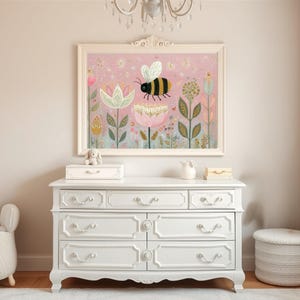 Pu&ograve; includere: Una stampa artistica incorniciata con un'illustrazione di un'ape sopra fiori colorati su sfondo rosa. L'opera d'arte &egrave; appesa sopra un com&ograve; bianco. La stanza &egrave; decorata in toni neutri, creando un'atmosfera calma e serena, ideale per una cameretta.