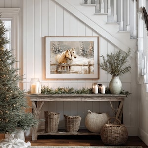 May include: A rustic wooden console table is decorated with a framed horse painting, candles, and woven baskets. A Christmas tree with fairy lights stands to the left. The scene is set against a white paneled wall and a staircase.