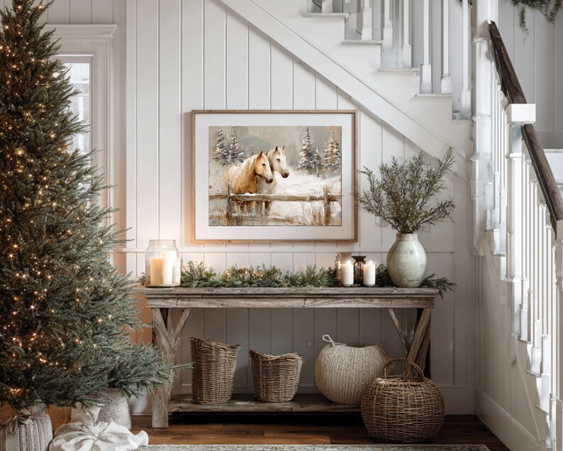 May include: A rustic wooden console table is decorated with a framed horse painting, candles, and woven baskets. A Christmas tree with fairy lights stands to the left. The scene is set against a white paneled wall and a staircase.