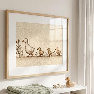 May include: A framed print featuring a watercolor illustration of a mother duck and her three ducklings walking in a line. The artwork has a neutral color palette with a beige background and a light wooden frame. The print is displayed in a nursery setting.