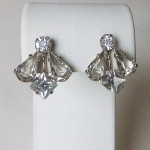 May include: A pair of silver tone clip-on earrings with clear faceted crystals. The earrings feature a large round crystal in the center, surrounded by smaller teardrop-shaped crystals.