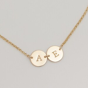May include: A gold chain necklace with two round pendants, one with the letter "A" and the other with the letter "E".