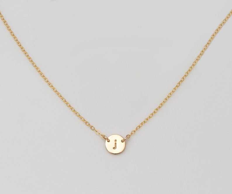 May include: A gold chain necklace with a small round pendant featuring the letter "J" engraved on it.