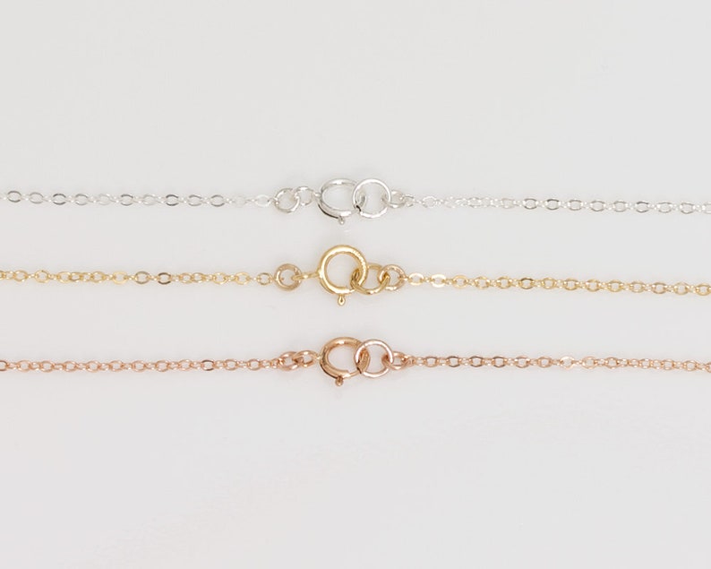 May include: Three delicate chains with lobster clasps. The chains are silver, gold, and rose gold.