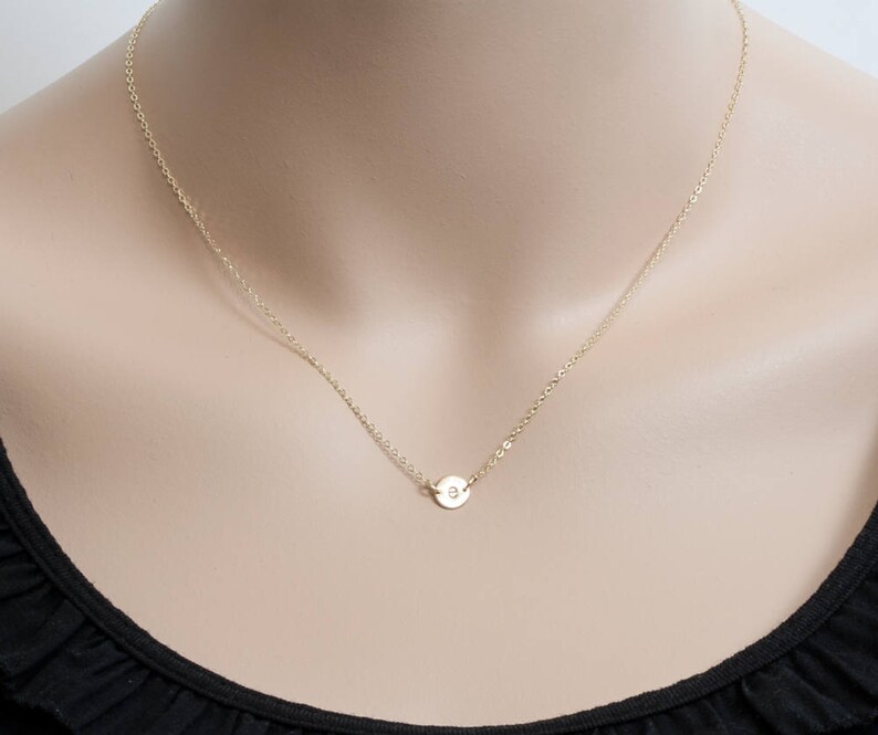 May include: A gold chain necklace with a small, round pendant featuring a single letter.