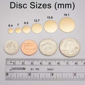 May include: A ruler with measurements in centimeters and inches, next to a set of gold-colored metal discs of varying sizes. The discs are labeled with their diameters in millimeters: 6.4 mm, 7 mm, 9.5 mm, 12.7 mm, 15.9 mm, and 19.1 mm.