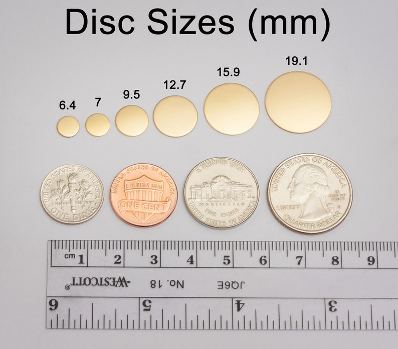 May include: A ruler with measurements in centimeters and inches, next to a set of gold-colored metal discs of varying sizes. The discs are labeled with their diameters in millimeters: 6.4 mm, 7 mm, 9.5 mm, 12.7 mm, 15.9 mm, and 19.1 mm.