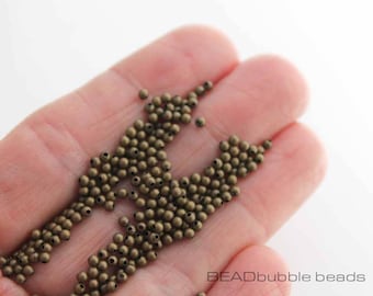 May include: A close-up of a hand holding a large quantity of small, round, bronze-colored beads. The beads are arranged in a loose pile, and some are spilling out of the hand.