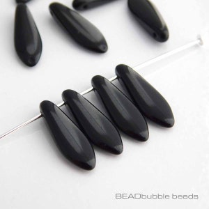 May include: Black glass beads in a teardrop shape, strung on a silver wire. The beads are glossy and have a smooth finish.