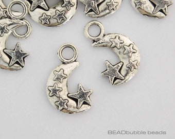 Op de afbeelding: Zilverkleurige metalen bedels in de vorm van een halve maan met een ster erop. De maan is versierd met kleinere sterren. De bedels hebben een springring om aan sieraden of andere knutselwerkjes te bevestigen.