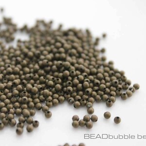 May include: A large pile of small, round, bronze-colored metal beads. The beads are scattered on a white surface.