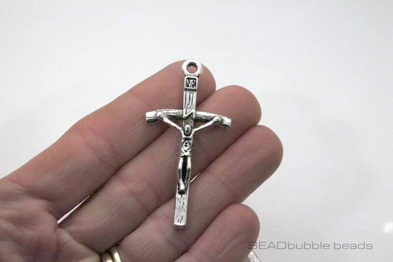 May include: Silver-toned metal crucifix charm with a detailed figure of Jesus Christ. The charm has a loop at the top for attaching to a necklace or bracelet.