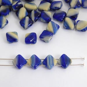 Può includere: Una collezione di perline quadrate in vetro blu e crema. Le perline hanno un aspetto marmorizzato, con i colori mescolati. Alcune perline sono infilate su fili argentati. Adatte per la creazione di gioielli e lavori artigianali.