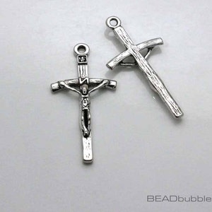 May include: Two silver metal cross charms. One cross charm features a detailed depiction of Jesus Christ on the cross. The other cross charm is a simple, plain cross.