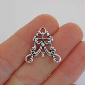 May include: A silver filigree charm with an elaborate, symmetrical design. The charm features a central bow-like element, curved lines, and small decorative beads. It has a loop at the top for attachment, suitable for jewellery making or crafting projects.