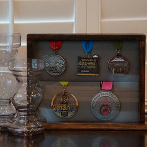 May include: A wooden shadow box display case with five medals inside. The medals are silver and have different designs. The shadow box is on a dark wood surface.