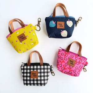 May include: Four small tote bags with brown leather handles and gold-colored clasps. The bags feature various patterns: yellow with strawberries, denim with strawberry appliques, black and white gingham, and pink floral. Each bag has a "tiny tote" label.