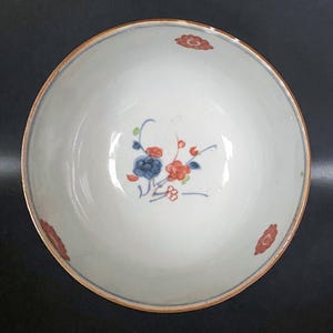 Puede incluir: Un cuenco de cer&aacute;mica blanca con un dise&ntilde;o floral en azul, rojo y verde. El cuenco tiene un borde marr&oacute;n.