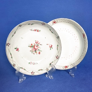 May include: Two white porcelain plates with a floral design. The smaller plate has a scalloped edge and a floral pattern with pink and red flowers. The larger plate has a scalloped edge and a floral pattern with pink and red flowers.