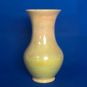 May include: A pale yellow ceramic vase with a pearlescent glaze. The vase has a wide mouth and a narrow base.