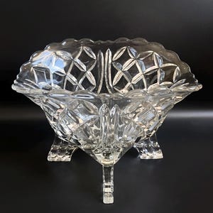 May include: A clear glass bowl with a scalloped edge and intricate diamond-shaped patterns. The bowl sits on three legs and is ideal for serving fruit or snacks.