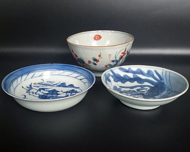 Puede incluir: Tres cuencos de cer&aacute;mica con dise&ntilde;os florales y de paisajes azules y blancos. Los cuencos est&aacute;n sobre un fondo negro.