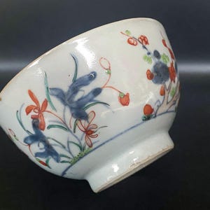 Puede incluir: Un cuenco de porcelana blanca con un dise&ntilde;o floral azul y rojo. El cuenco tiene un borde ligeramente acampanado y una base redondeada.