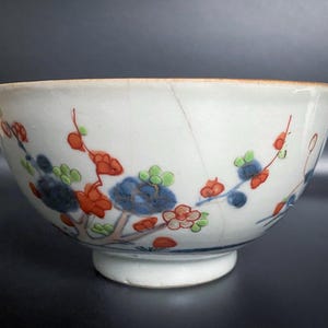 Puede incluir: Un cuenco de porcelana blanca con un dise&ntilde;o floral en azul, rojo y verde. El cuenco tiene un borde ligeramente acampanado y una base redondeada.