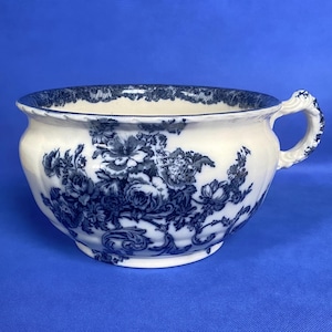 May include: A white ceramic chamber pot with a blue floral design and a handle.