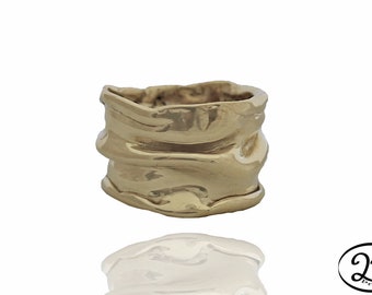 May include: A gold-toned ring with a textured, wavy design. The ring is thick and has a wide band.
