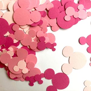 Peut inclure: Une collection de confettis roses et rose clair en forme de Mickey Mouse, dispersés sur une surface blanche. Les confettis varient en taille et en teinte, créant un effet de superposition. Idéal pour les décorations de fête ou les projets d'artisanat.