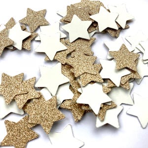 Op de afbeelding: Een verzameling stervormige confetti in goudglitter en wit. De confetti is verspreid, wat een feestelijke uitstraling creëert, geschikt voor knutselwerkjes of decoraties. Elke ster meet ongeveer 2 cm.