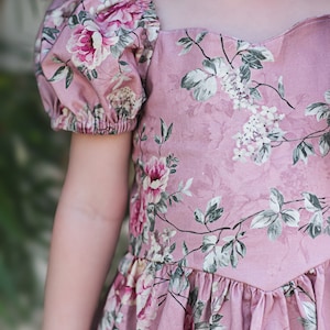 Pu&ograve; includere: Un abito rosa floreale con maniche a sbuffo e scollatura a cuore. L'abito ha un design di ispirazione vintage con uno schema floreale.