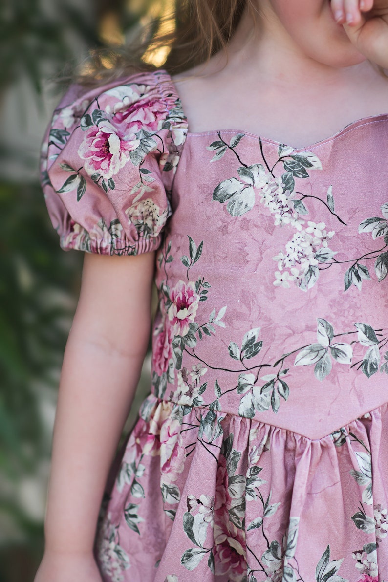 Pu&ograve; includere: Un abito rosa floreale con maniche a sbuffo e scollatura a cuore. L'abito ha un design di ispirazione vintage con uno schema floreale.