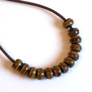 May include: A brown leather cord necklace with brown and gold striped wooden beads.
