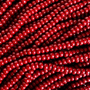 May include: A close-up of a strand of red glass beads. The beads are small and round, and they are arranged in a tight, even pattern.