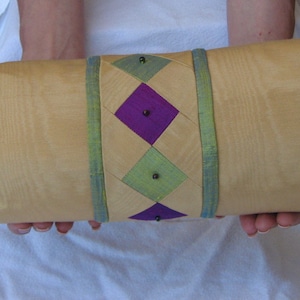 May include: A yellow cylindrical pillow with purple and green diamond-shaped patterns. The pillow is decorated with black beads.