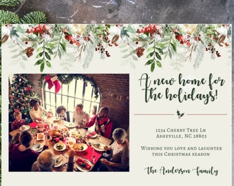 May include: A Christmas card with a watercolor border of greenery and red berries. The card features a photo of a family gathered around a table for a holiday meal. The text reads "A new home for the holidays!" and includes the family's address and a holiday greeting.