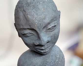 May include: A gray clay sculpture of a person's head and shoulders. The sculpture has a realistic face with a thoughtful expression.