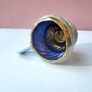 Könnte beinhalten: Eine kleine, blaue Keramiktasse mit goldfarbenem Rand. Die Tasse ist mit einem blauen und goldenen Wirbelmuster verziert.