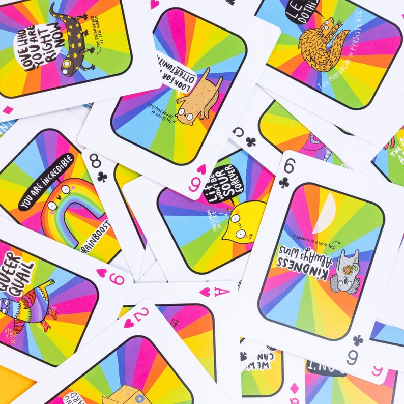 A pack of playing cards with a rainbow smiling on the front illustrated by Katie Abey. It is on a yellow background with confetti