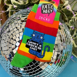 Katie Abey What a Crock of Shit socks with blue cat holding a sign. They are rainbow striped and lovely and vibrant.