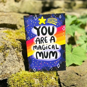 The front cover is a dark blue to black galaxy background with various red, white, yellow stars and sparkles, a red, orange, yellow gradient stripes going across the centre. The text reads You are a magical mum with a yellow shooting star above it.