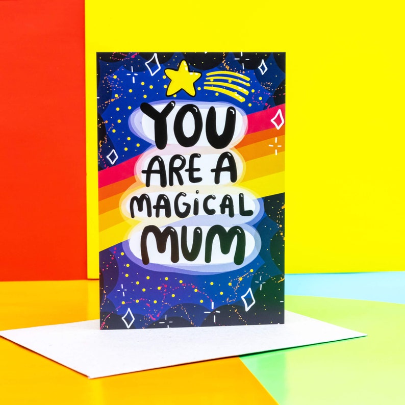 The front cover is a dark blue to black galaxy background with various red, white, yellow stars and sparkles, a red, orange, yellow gradient stripes going across the centre. The text reads You are a magical mum with a yellow shooting star above it.