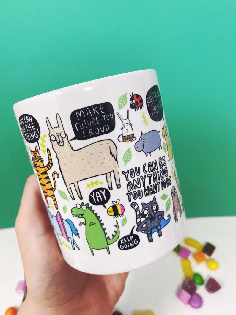 A white ceramic mug with lots of Katie Abey fun illustrations on telling you that you can do it. Text says the Mug of Motivation