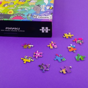 puzzle box with pieces next to it featuring illustrations by Katie Abey on a purple background