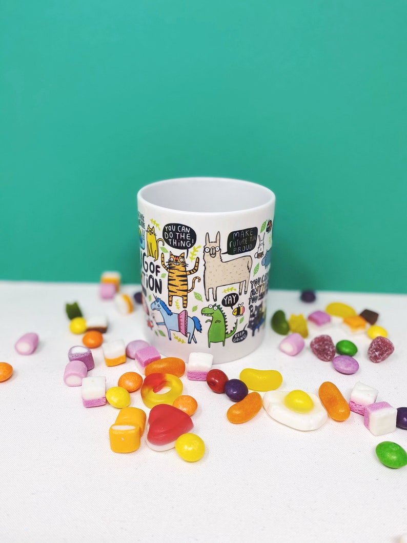 A white ceramic mug with lots of Katie Abey fun illustrations on telling you that you can do it. Text says the Mug of Motivation