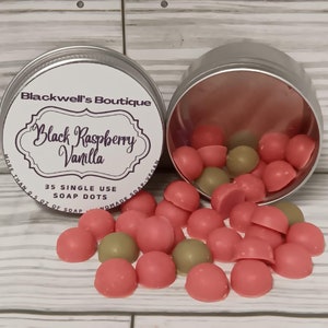 May include: A silver tin with a label reading "Blackwell's Boutique Black Raspberry Vanilla" next to another open tin spilling out pink and green soap dots. The label also says "35 Single Use Soap Dots".
